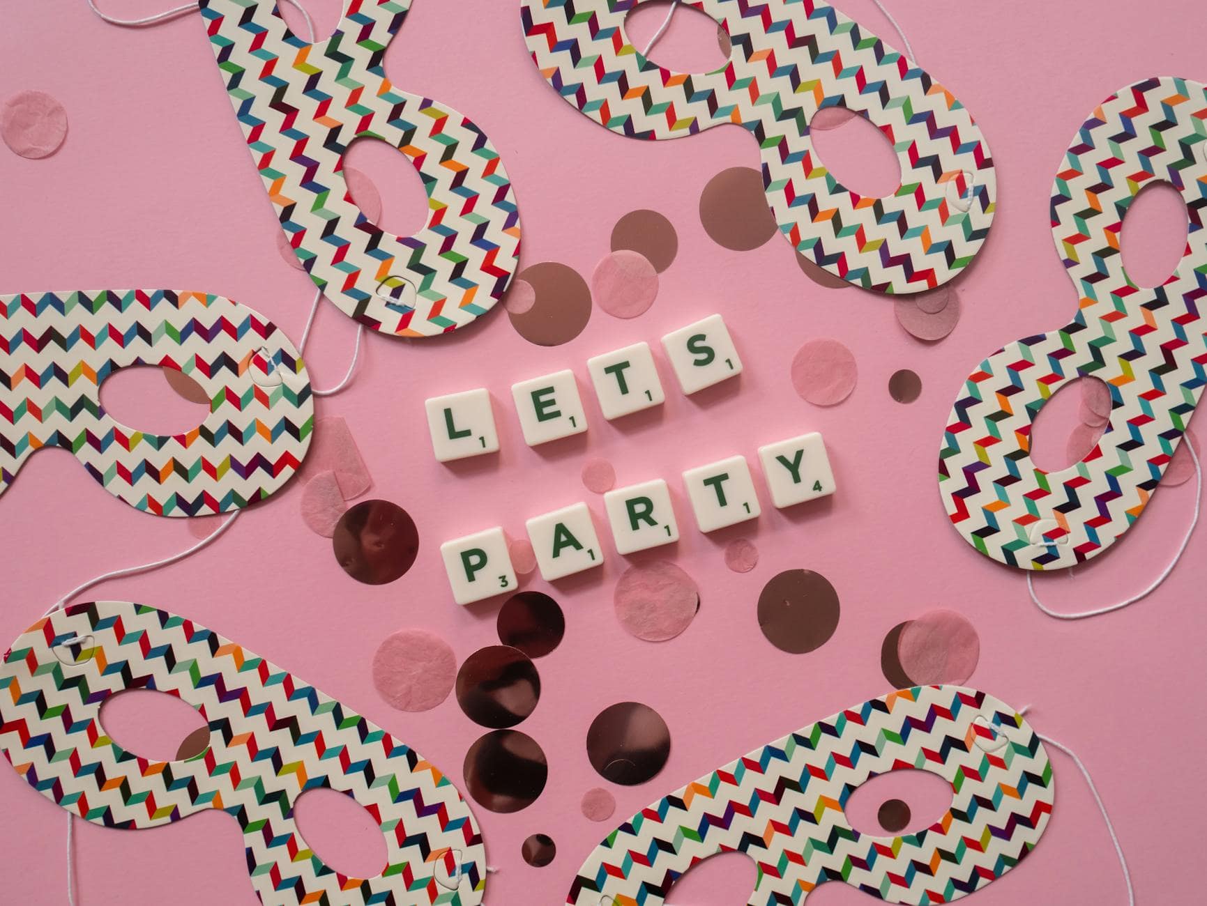 Flat lay of themed party masks and 'Let's Party' text on a pink surface.